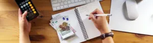 Por que priorizar o pagamento das dívidas: fotografia de uma pessoa escrevendo e fazendo contas em uma calculadora.