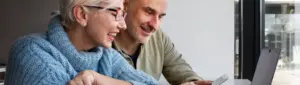 Primeira parcela 13º salário INSS: fotografia de um casal de idosos usando o computador e o celular.