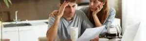 Pior momento para negociar dívidas: fotografia de um homem e uma mulher preocupados olhando para documentos de dívidas.