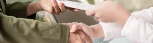 Portabilidade de dívida: fotografia de duas pessoas apertando as mãos. Uma está entregando um documento para outra.