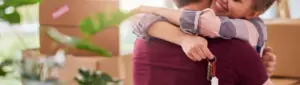 Financiamento imobiliário: fotografia de um casal se abraçando enquanto a mulher segura as chaves de uma casa.