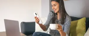 Saldo FGTS: fotografia de uma mulher sorrindo enquanto olha para o celular.