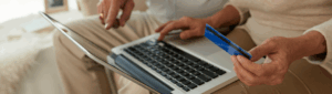 Empréstimo consignado: fotografia de um casal de idosos segurando um cartão de crédito e usando o notebook.