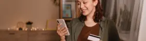 Cashback: fotografia de uma mulher sorrindo enquanto segura um celular e um cartão.