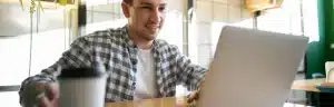 Dívida Banco Mercantil: fotografia de um homem sorrindo enquanto usa o computador.