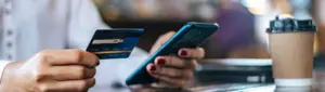 Cashback ou milhas: fotografia de uma pessoa segurando um cartão de crédito e um celular.