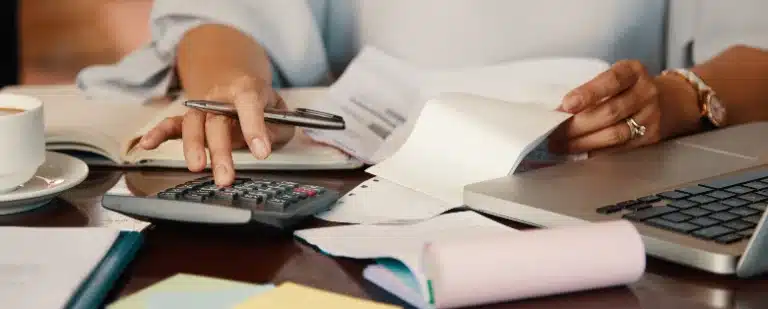 Como limpar nome: fotografia de uma pessoa segurando faturas e digitando na calculadora.