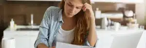 Dívida Banco do Brasil: fotografia de uma mulher olhando com expressão de preocupação para uma conta em papel em sua mão.