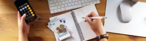 Orçamento pessoal: fotografia de uma pessoa usando uma calculadora e escrevendo em um caderno.