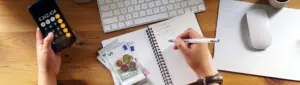 Hábitos financeiros saudáveis: fotografia de uma pessoa fazendo contas com a calculadora e em um caderno.