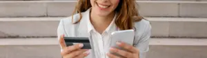 Inteligência financeira: fotografia de uma mulher sorrindo enquanto segura um celular e um cartão de crédito.