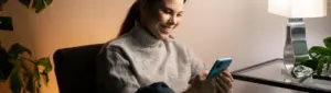 Negociação Pitágoras: fotografia de uma mulher sorrindo enquanto usa o celular.