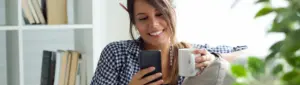 Poupança Social Digital: fotografia de mulher sorrindo enquanto usa o celular.