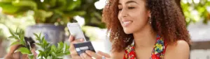 Como cancelar compra no cartão de crédito: fotografia de uma mulher sorrindo enquanto segura um cartão e um celular.