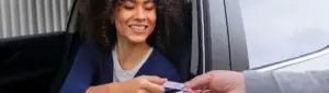 Como pagar licenciamento atrasado: fotografia de uma mulher sorrindo e entregando a CNH para outra pessoa.