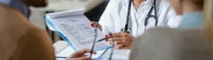 Dívida com plano de saúde: fotografia de uma médica apontando para um documento para um casal.